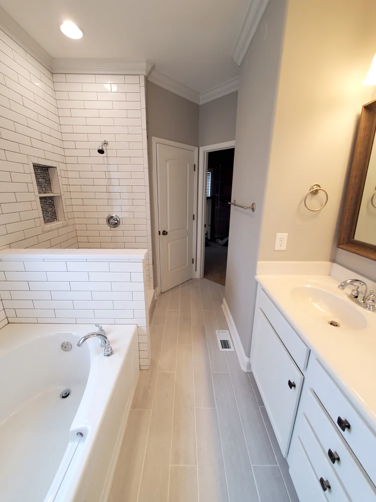 Bathroom with jetted drop-in tub, white subway tile shower wall with mosaic niche and white vanity
