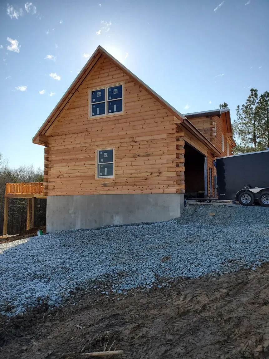 Gable end of a log-sided home on a poured concrete foundation, with an unfinished door opening in the attached wing