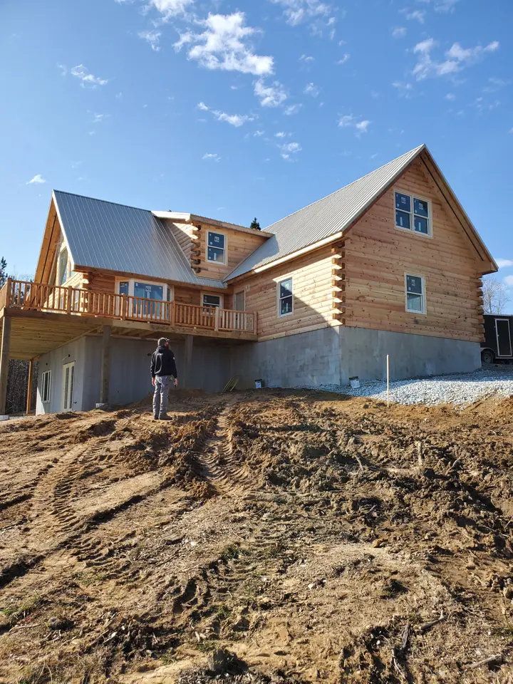 Log home under construction with a standing-seam metal roof, open elevated deck, and exposed walkout foundation