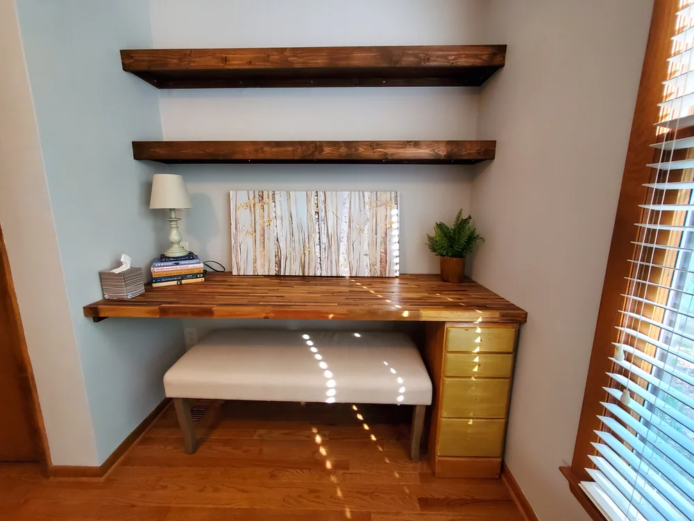 Built-in desk with butcher block top, dark-stained floating shelves and a bench in a window nook