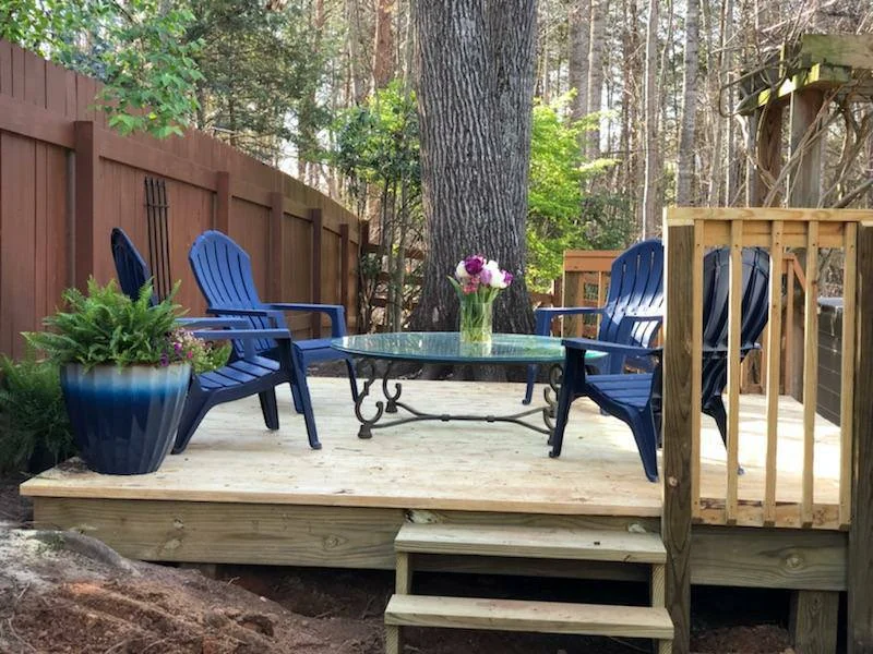 Low backyard deck in knotty pressure-treated wood with Adirondack chairs and a partly built railing