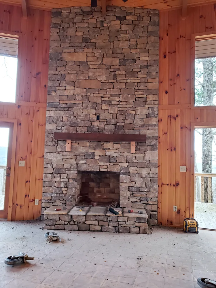Floor-to-ceiling dry-stacked stone fireplace with wood mantel in a knotty pine great room under construction