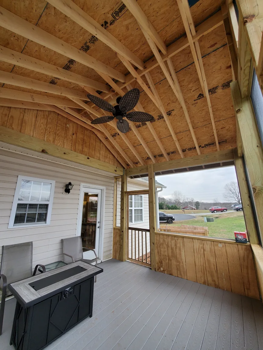 Screened porch under construction with exposed rafters and OSB roof deck, ceiling fan, and gray composite decking