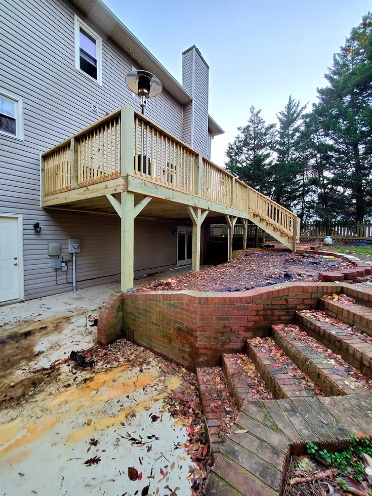 Elevated pressure-treated wood deck with baluster railing and long stair run at the back of a two-story home