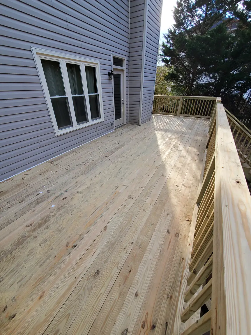 Backyard wood deck with weathered decking and newly built pressure-treated railing along a gray-sided house