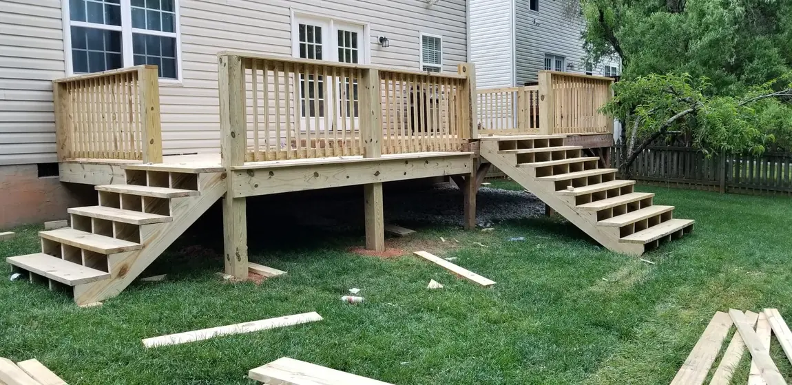 New pressure-treated deck with railings and two sets of stairs off the back of a house