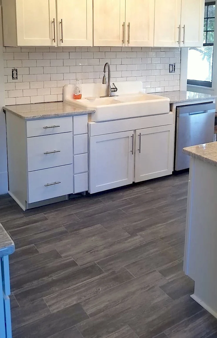 White shaker kitchen with apron-front farmhouse sink, subway tile backsplash, stone counters, wood-look tile floor
