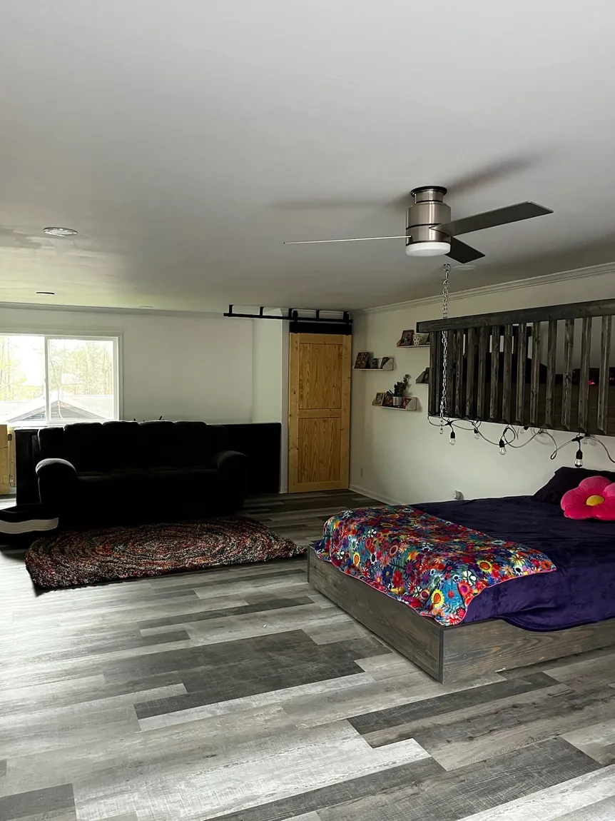 Finished open bedroom and lounge with gray plank flooring, ceiling fan, sliding barn door, and loft railing