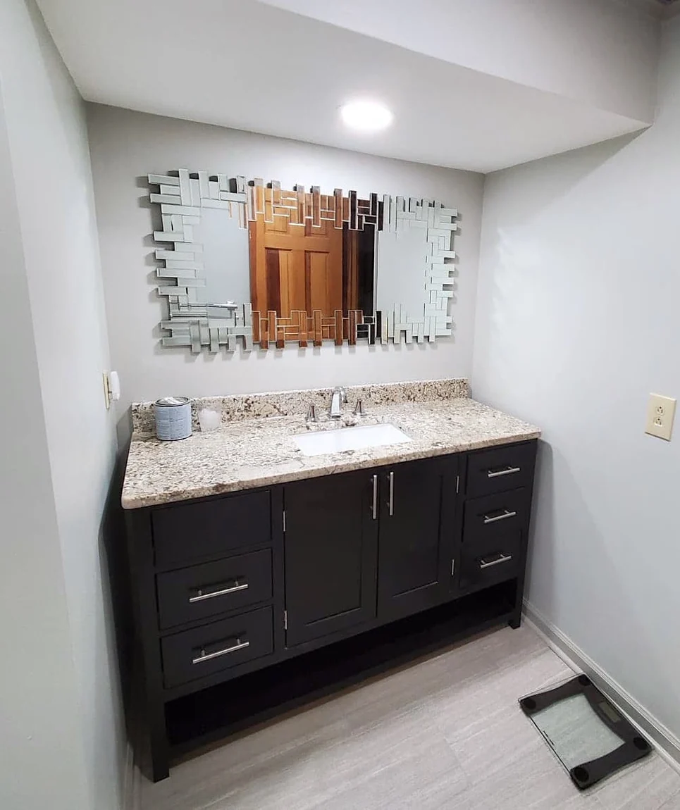 Bathroom vanity area with dark shaker cabinet, granite top, undermount sink, and large geometric mirror