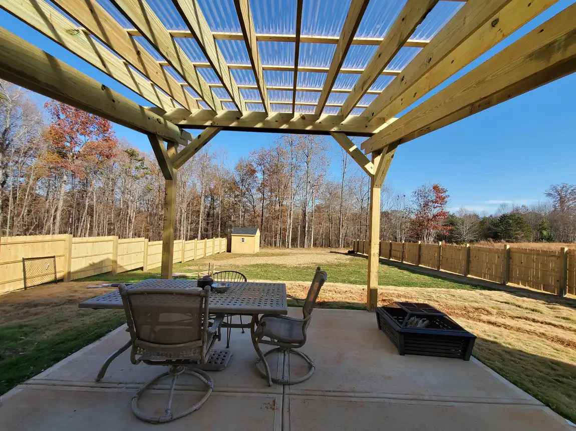 Pressure-treated pergola with clear corrugated roof panels over a poured concrete patio with fire pit