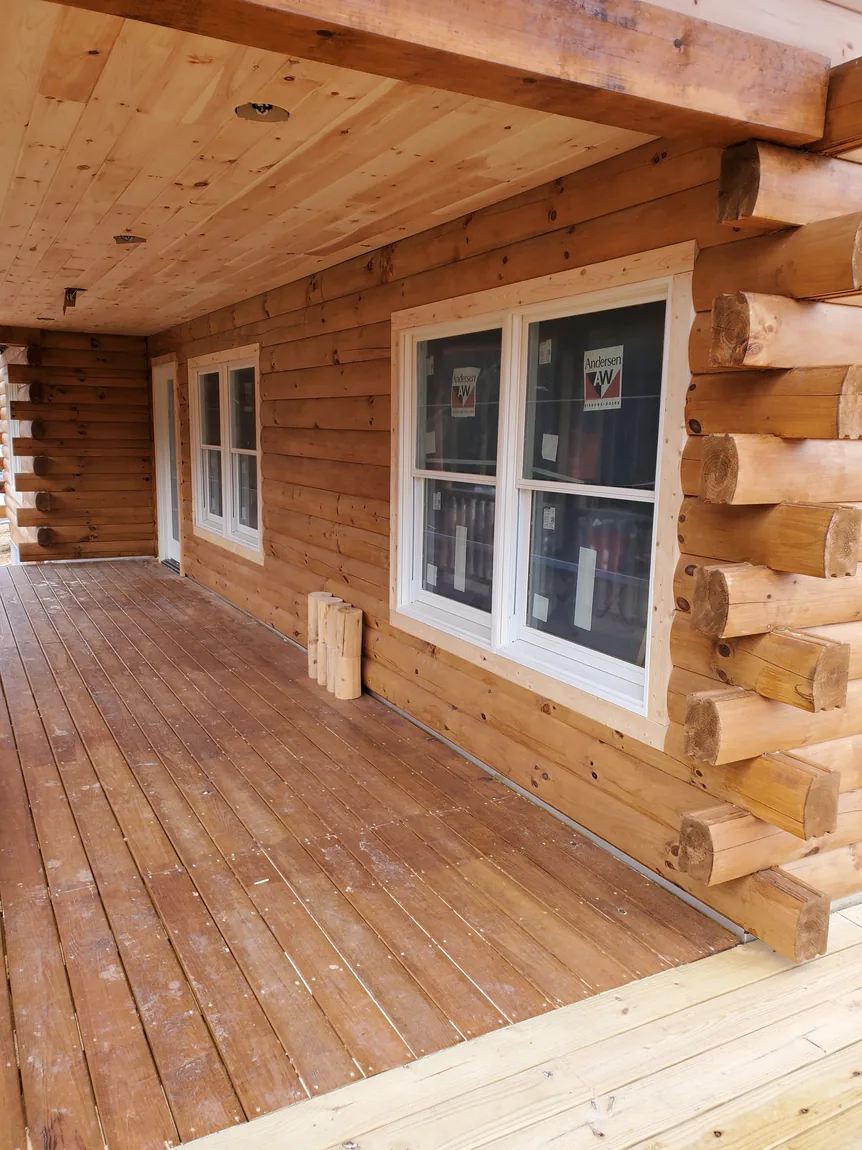 Covered porch of a log-sided home with new double-hung windows still carrying factory labels