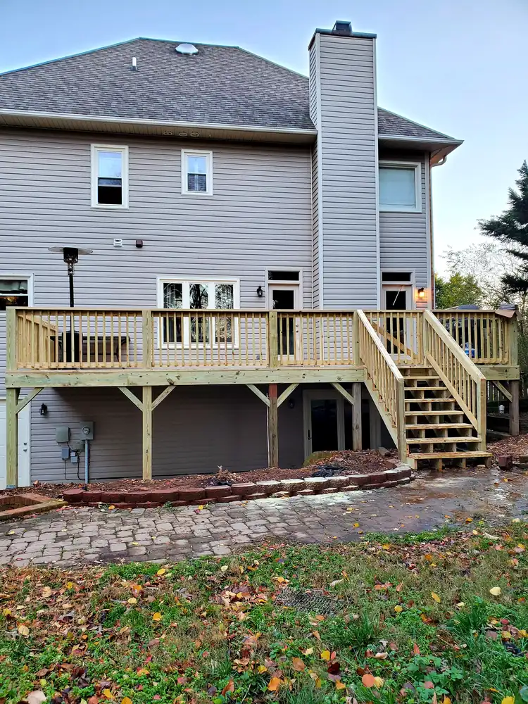 New pressure-treated deck with railings and stairs on the back of a two-story home above a paver patio