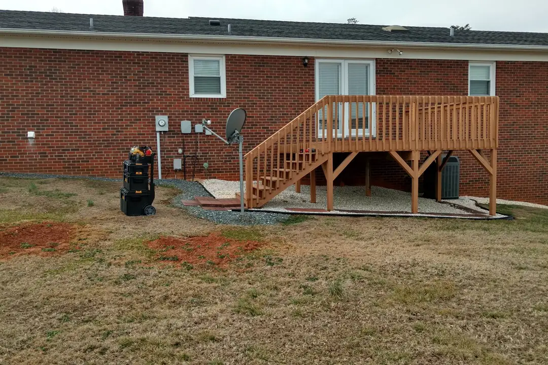Newly built pressure-treated deck with stairs and railings on the back of a brick ranch home