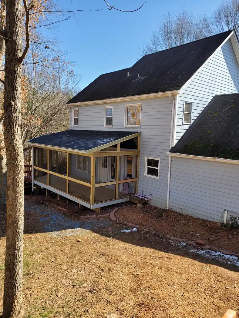 Screened porch under construction on a two-story home, bare framing exposed and screens partly installed