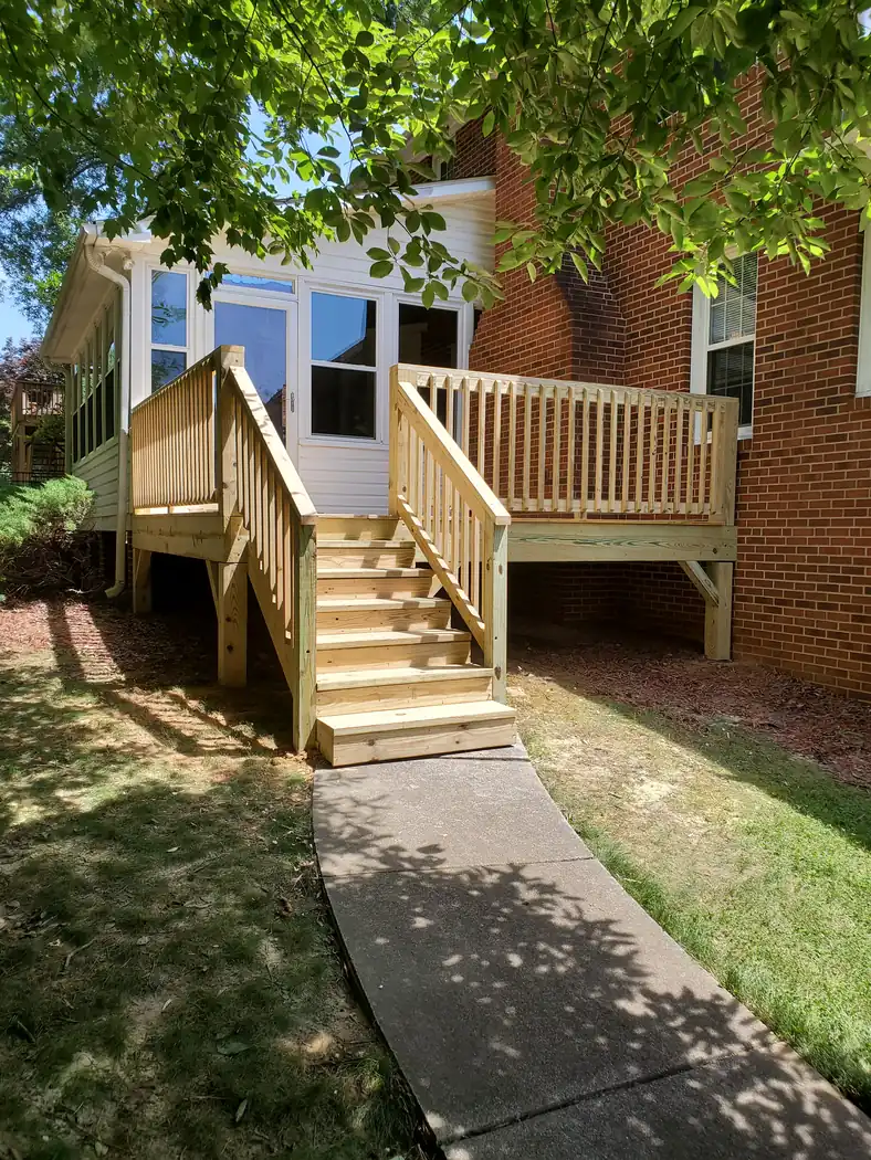 New pressure-treated deck with railings and steps beside a white enclosed porch on a brick home