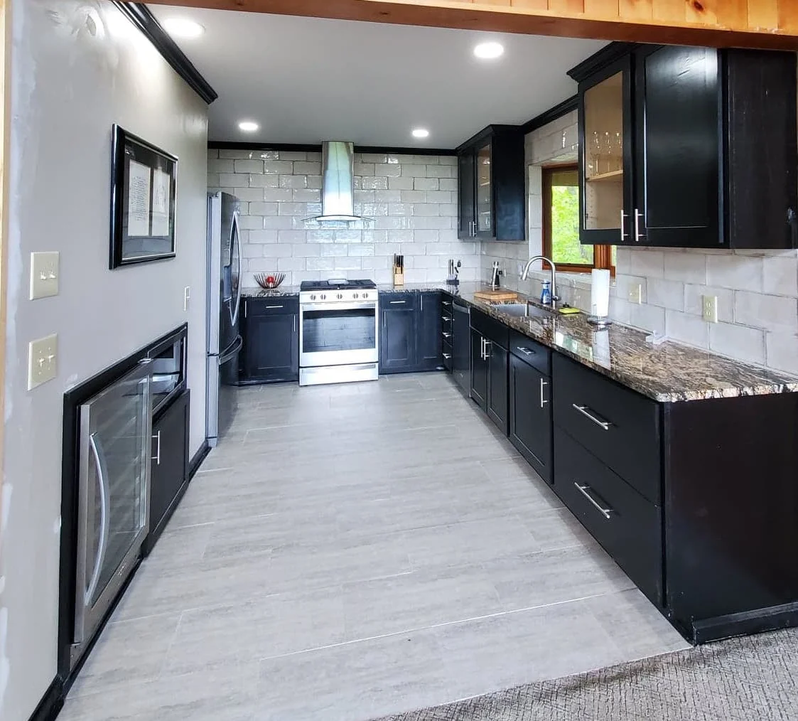 Finished kitchen with black cabinetry, veined granite counters, white subway tile backsplash and stainless range hood