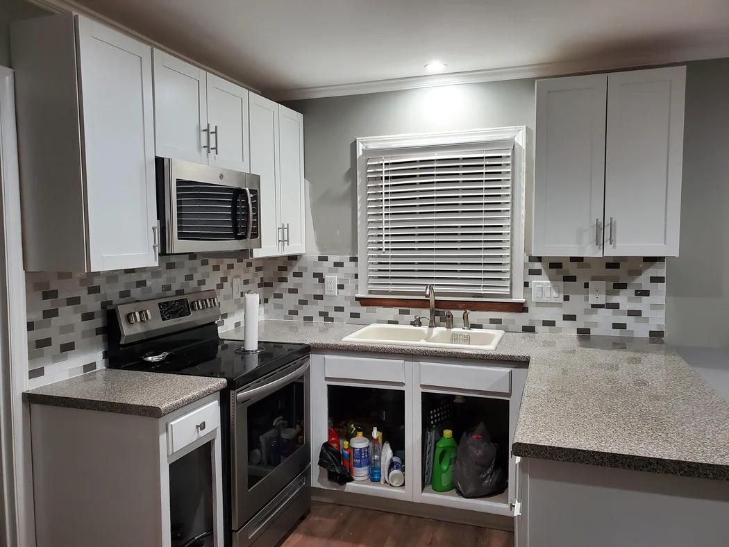 Kitchen with white shaker cabinets, multi-tone mosaic tile backsplash, and speckled stone-look counters