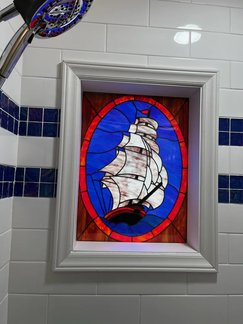 Stained glass sailing ship window set in a subway tile shower wall with cobalt blue accent tiles