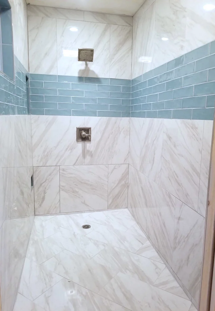 Walk-in shower tiled in white marble-look large-format tile with a teal glass subway accent band