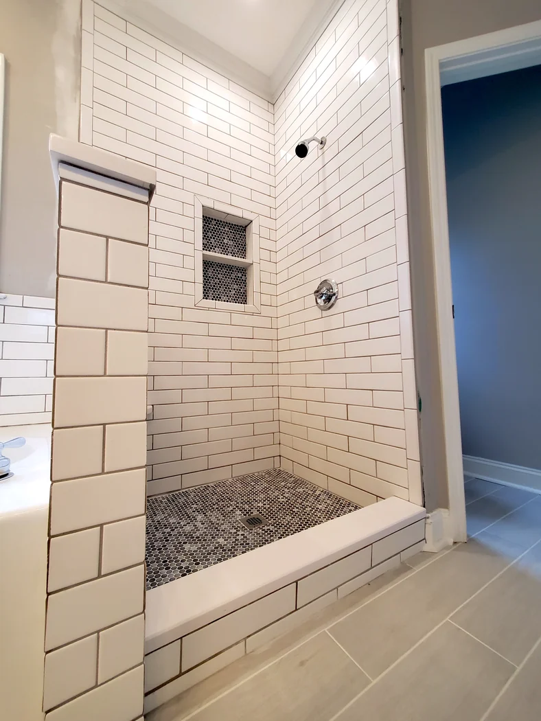 Walk-in tile shower with white subway walls, penny-round mosaic floor, and a recessed niche