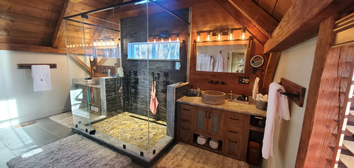 Finished bathroom with frameless glass walk-in shower, dark ledger tile, pebble floor and rustic wood vanity