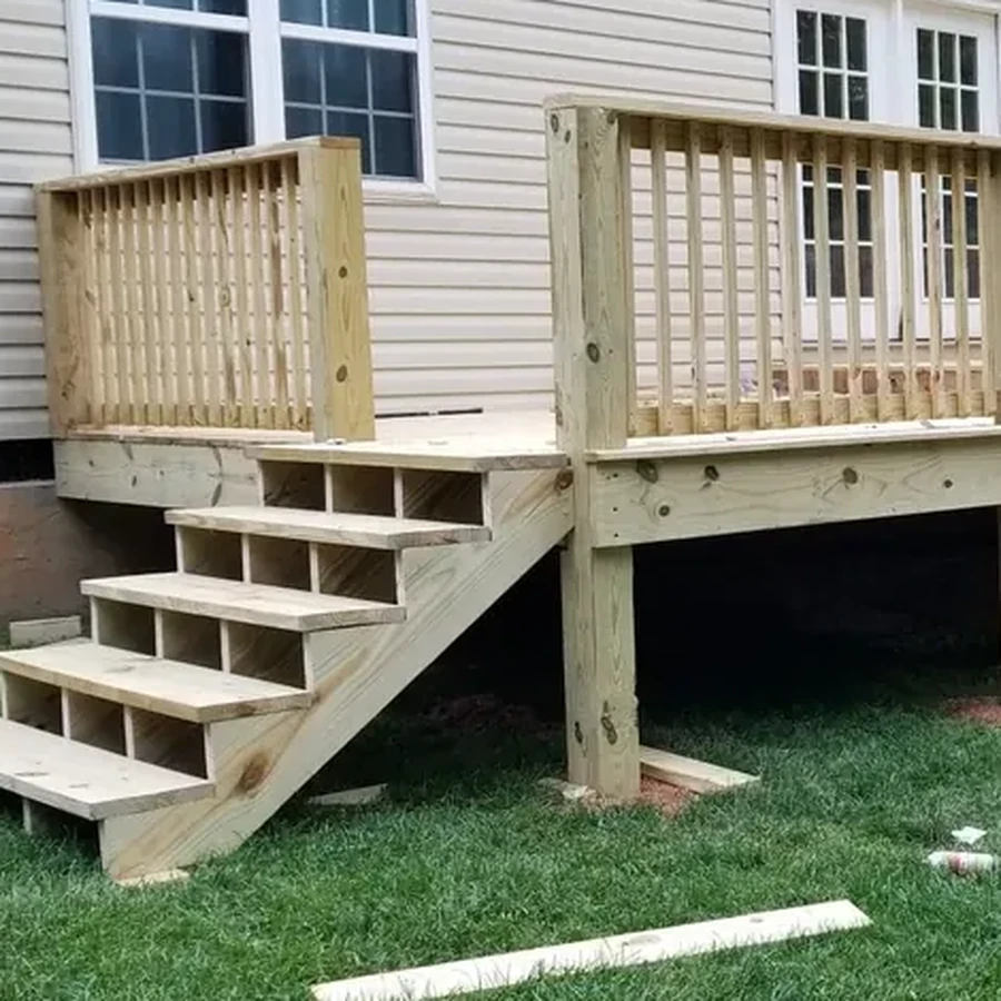 New pressure-treated deck with railings and open-stringer stairs attached to a vinyl-sided house