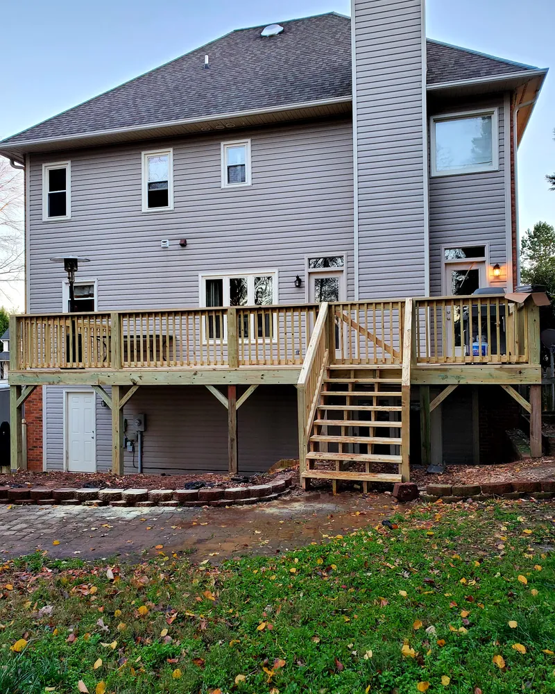 Newly built raised pressure-treated deck with wood railings and stairs down to a brick paver patio