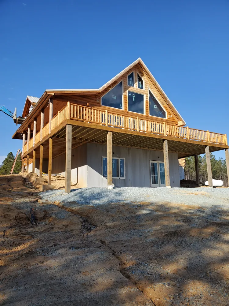 New home under construction with log-look siding, tall gable windows and an elevated wraparound deck