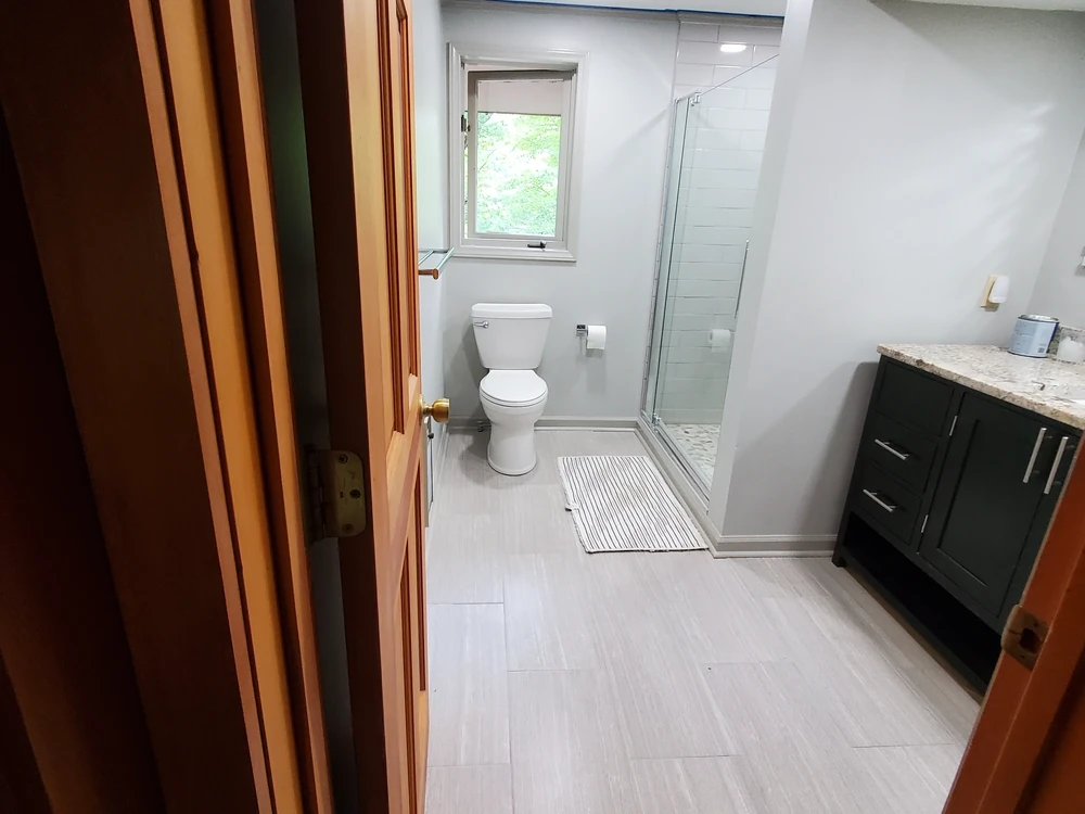 Remodeled bathroom with a corner glass shower, subway tile, toilet and a dark vanity with stone countertop