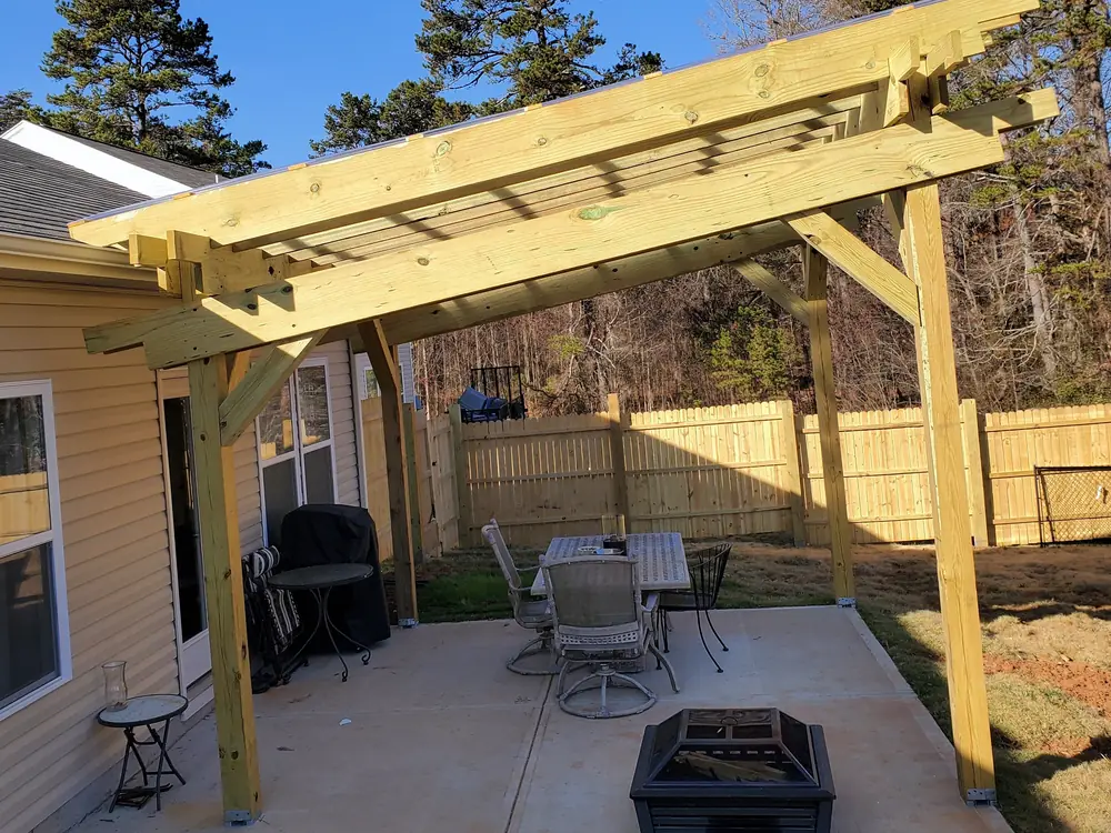 Attached pressure-treated pergola shading a concrete patio with a dining set and fire pit