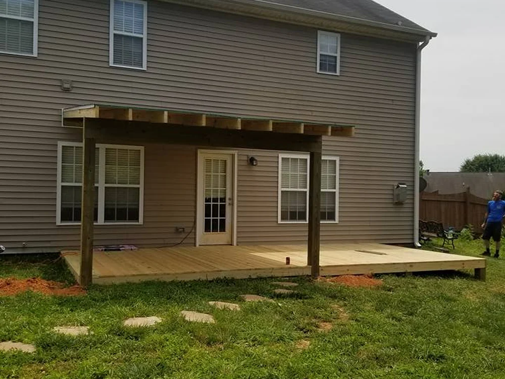 Low pressure-treated wood deck with a newly framed and sheathed shed roof cover at a two-story home