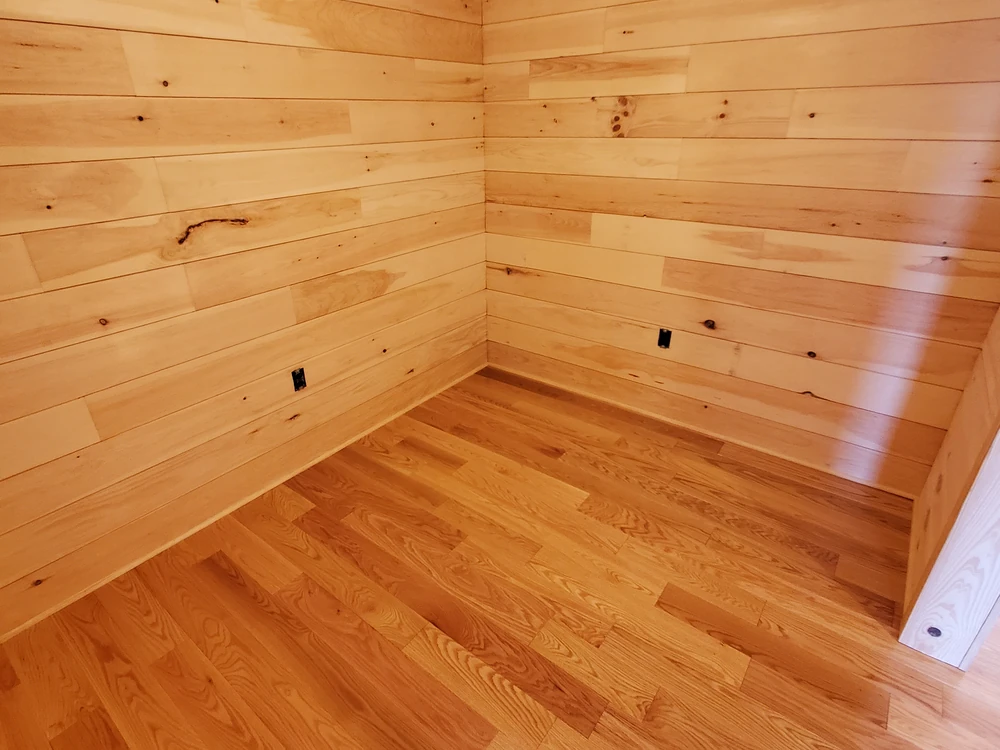 Corner of an empty room with knotty wood plank walls and new hardwood flooring, trim still to come
