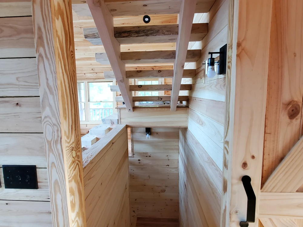 Interior stair landing with knotty pine plank walls, open stair treads overhead, and a black wall sconce