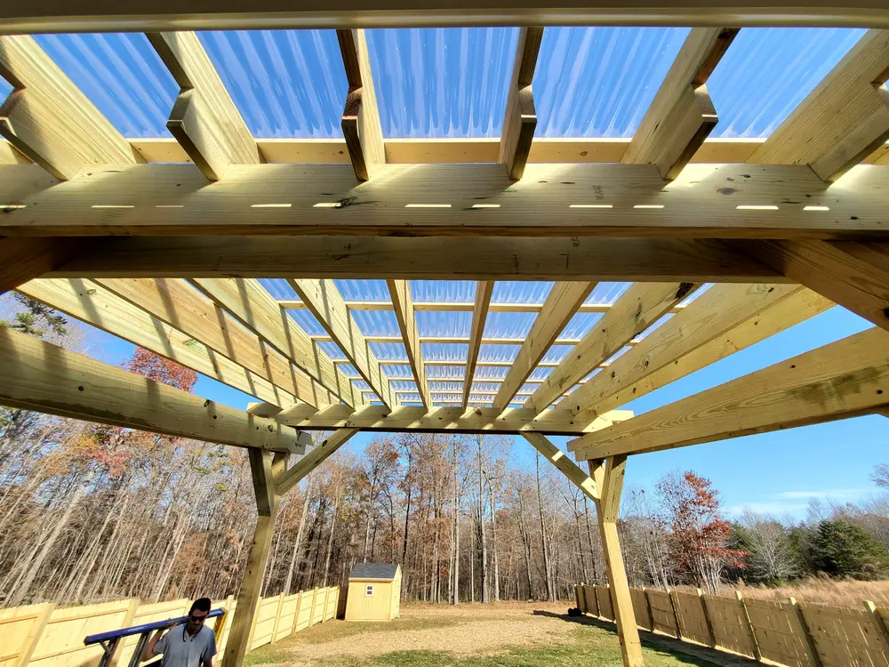 Pressure-treated pergola with clear corrugated roof panels over a fenced backyard