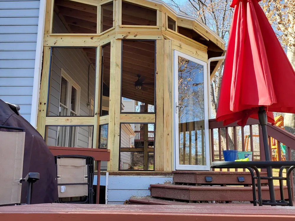 Newly built screened porch in bare pressure-treated framing with a glass door, set on an existing deck