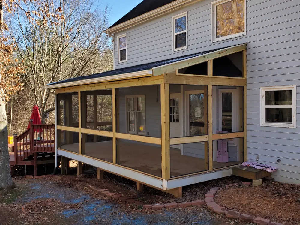 Screened porch addition under construction with new pressure-treated framing and screens