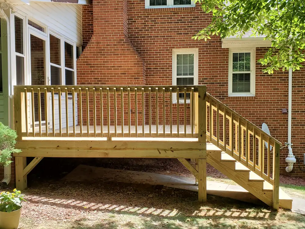 New pressure-treated deck with railings and stairs built off a brick home