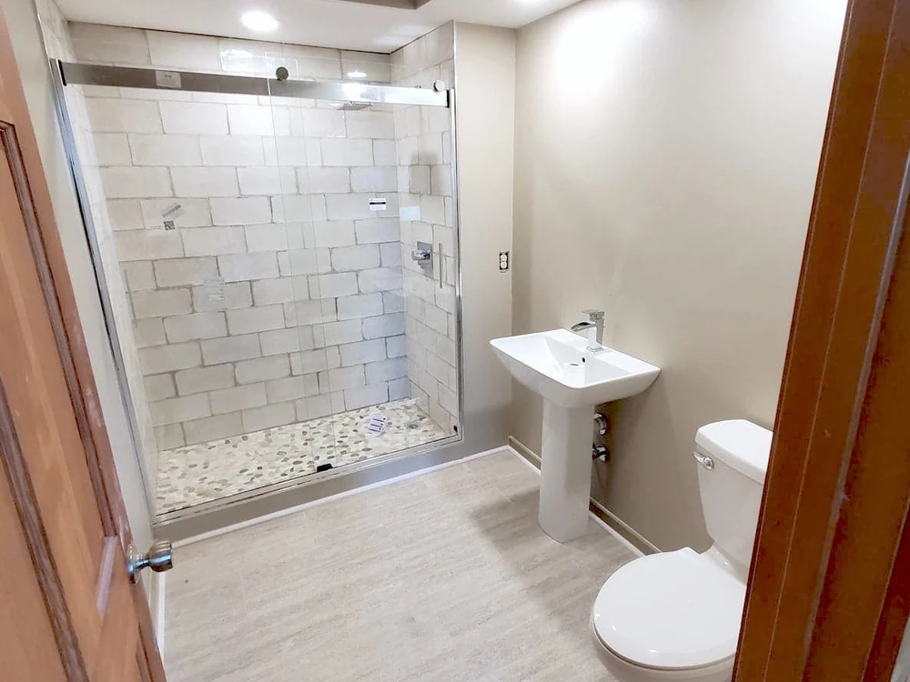 Bathroom remodel with a tile walk-in shower, glass door, and pedestal sink