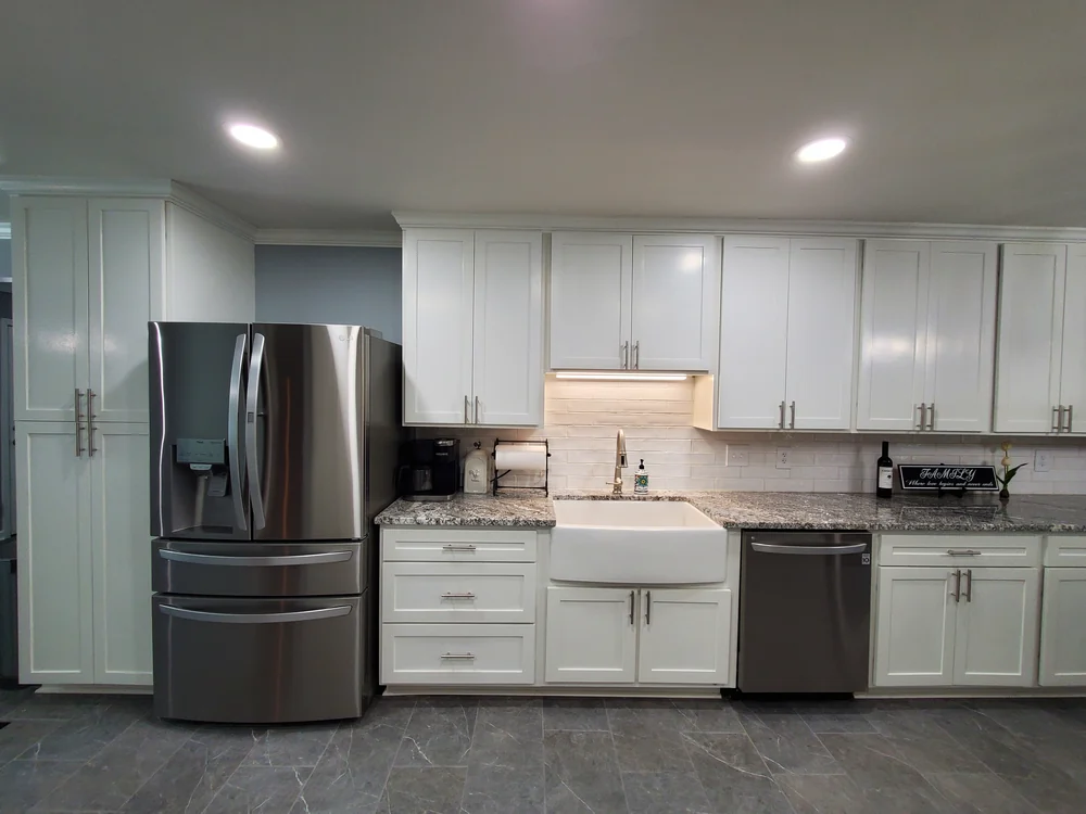 Kitchen with white shaker cabinets, apron-front farmhouse sink, speckled stone counters and tile backsplash