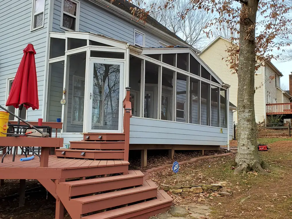 Older glass-and-screen porch enclosure with white frames on a gray-sided two-story home, before rebuild