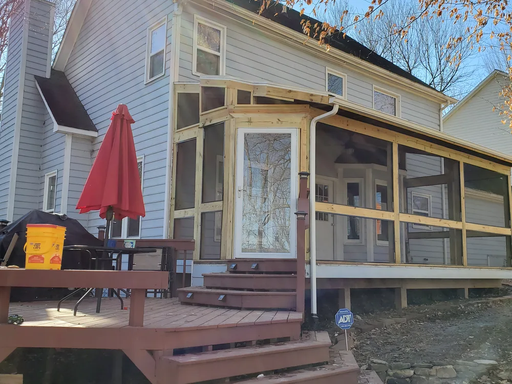 Same porch mid-rebuild with new raw framing lumber and screen panels installed, trim and finish still to come