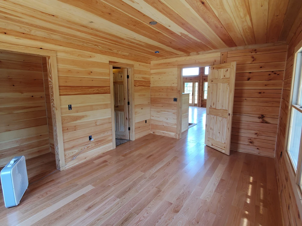 Empty room lined in knotty pine tongue-and-groove walls and ceiling with glossy hardwood plank flooring